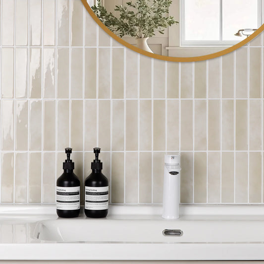 Bathroom wall above the washbasin covered with glossy beige tile stickers and a round gold mirror