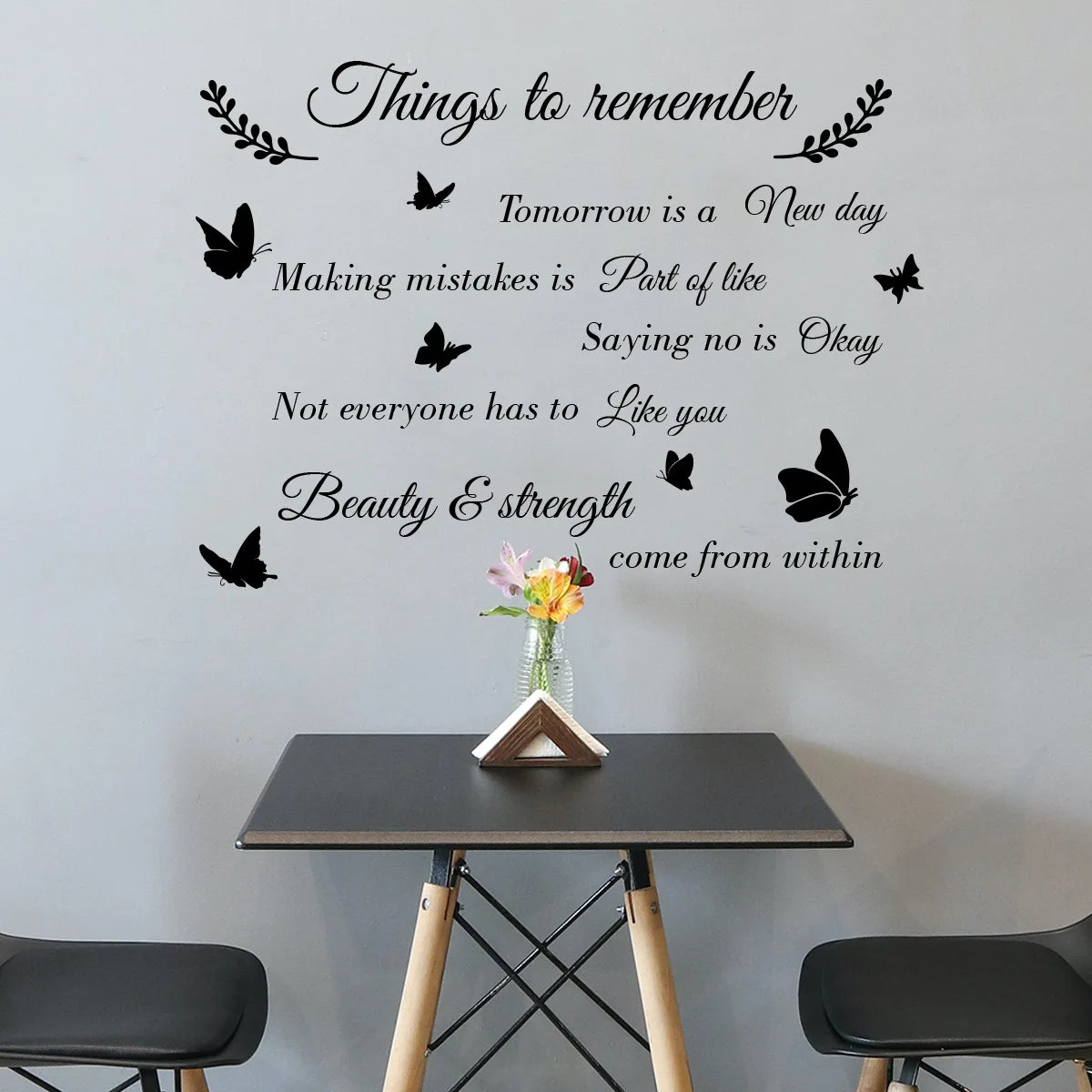 Black phrase sticker with butterflies on a grey wall above a black side table with flowers