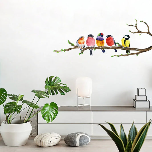 Muursticker met vogels op een tak, geplaatst op een wit laag kastje met planten