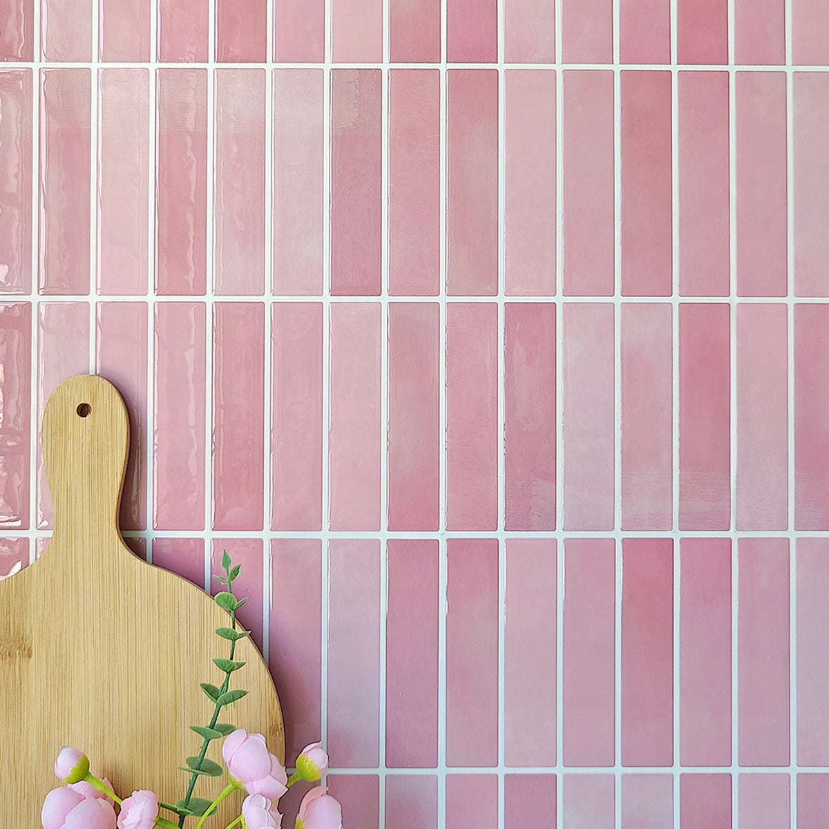 Pink wall with rectangular tile stickers, a wooden chopping board and some flowers