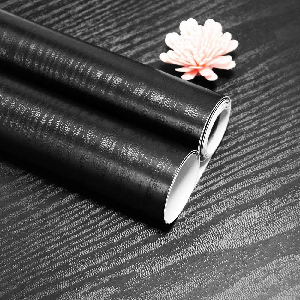 Two rolls of black wood effect vinyl on a covered surface, showing the embossed grain