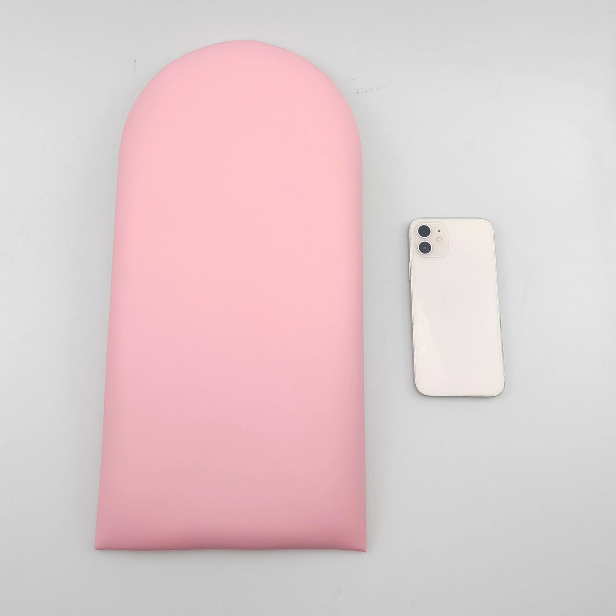 Roze gestoffeerd paneel met een boogvormige bovenrand op een grijze achtergrond, naast een telefoon als maatvergelijking