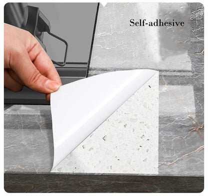 Schutzpapier wird von der Rückseite einer grauen Klebefolie in Marmoroptik auf einer Arbeitsplatte abgezogen