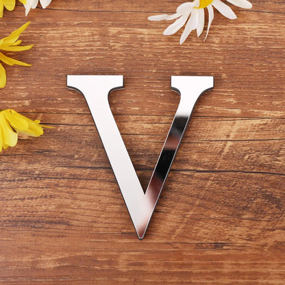 Letter V in silver mirror acrylic, 20 cm, on a wooden table with flowers