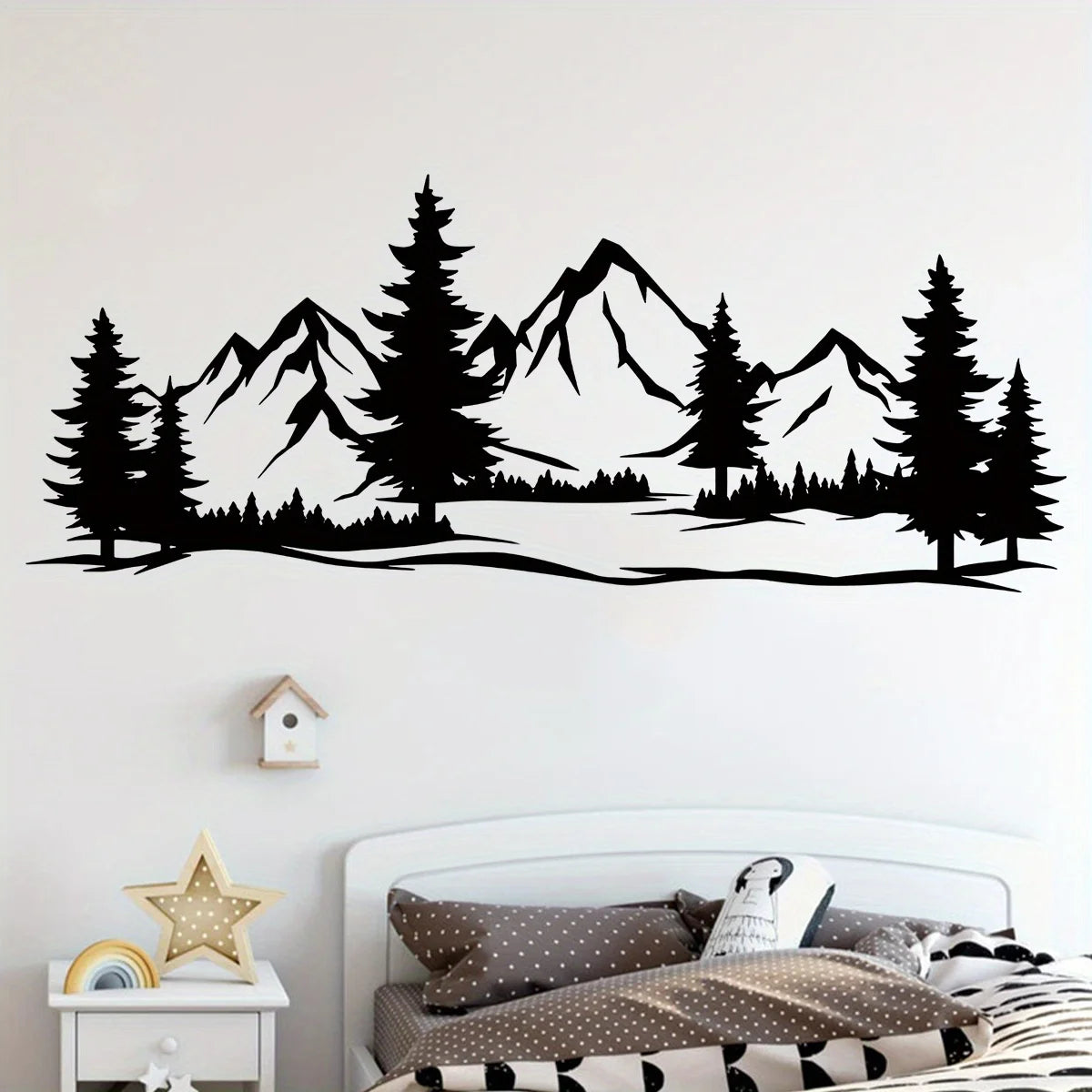 Mountain and pine sticker in black above the headboard of a bed in a children’s room