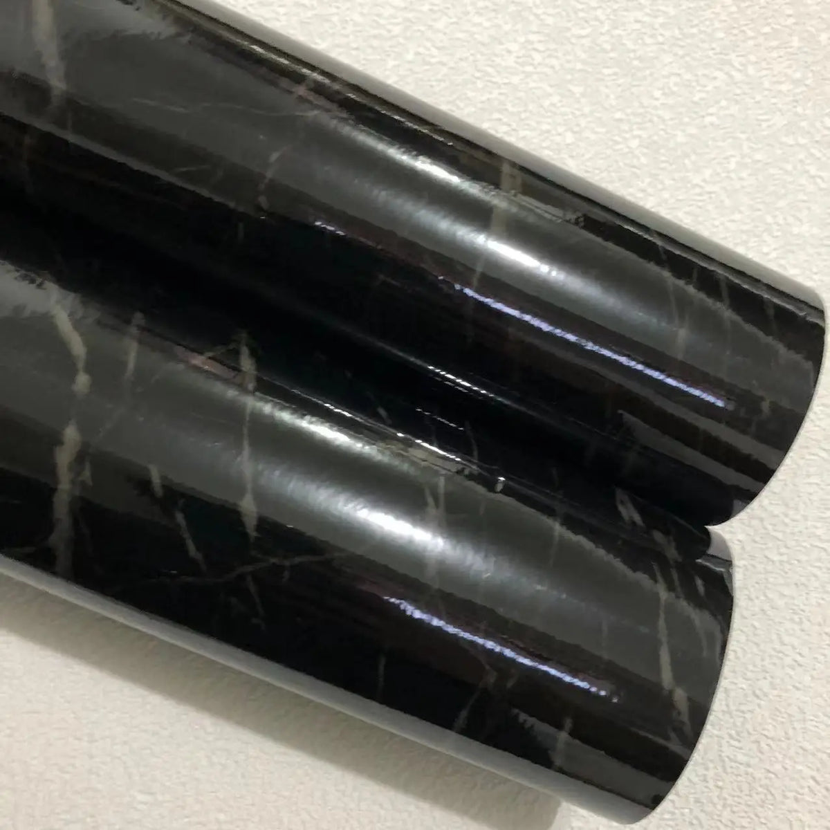 Zwei Rollen glänzende schwarze Klebefolie in Marmoroptik mit hellen Adern