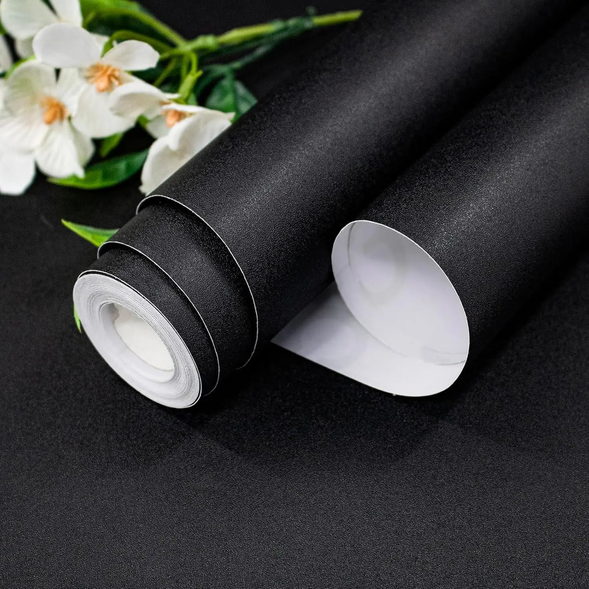 Zwei Rollen schwarze Möbelfolie mit weißer Rückseite und weißen Blumen