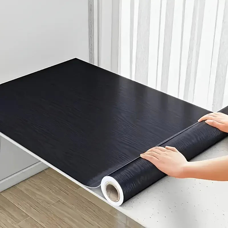 Black wood effect adhesive vinyl being laid over a table top during fitting