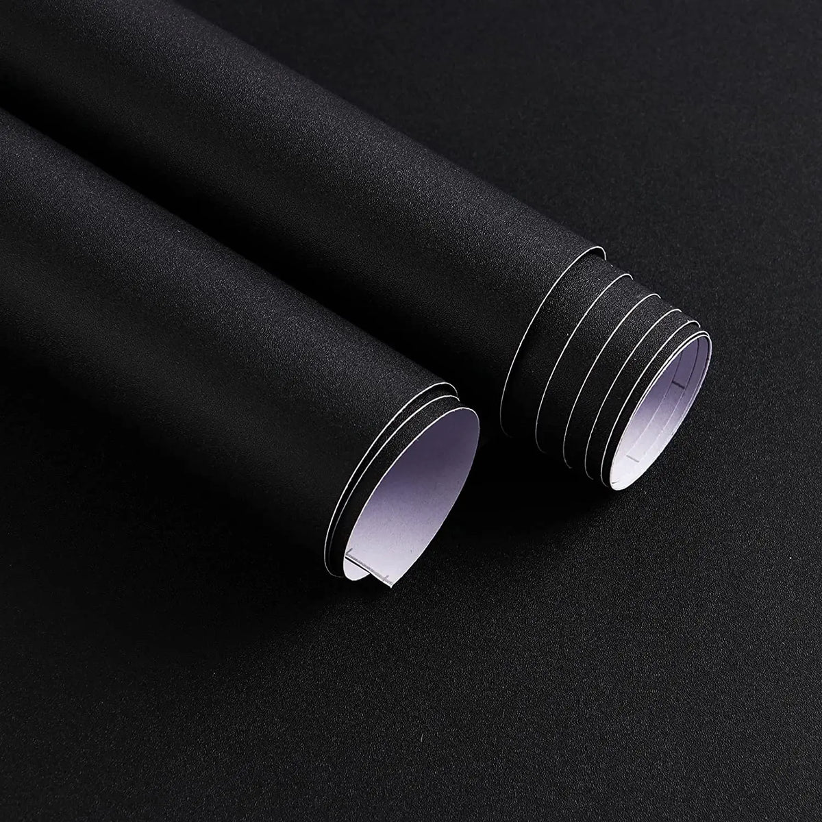 Zwei Rollen matte schwarze selbstklebende Folie, eine geöffnet, mit weißem Schutzpapier auf der Rückseite