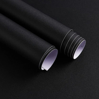 Zwei Rollen matte schwarze selbstklebende Folie, eine geöffnet, mit weißem Schutzpapier auf der Rückseite