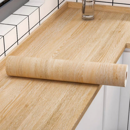 Roll of honey yellow wood effect adhesive vinyl on a covered worktop, in front of white tiles
