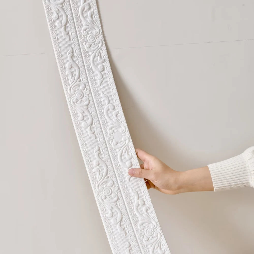 A hand rests the white raised moulding against a light wall