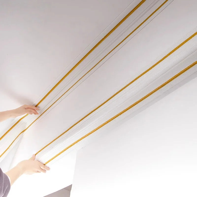 Two hands fit self-adhesive strips with gold lines along the top edge of a ceiling