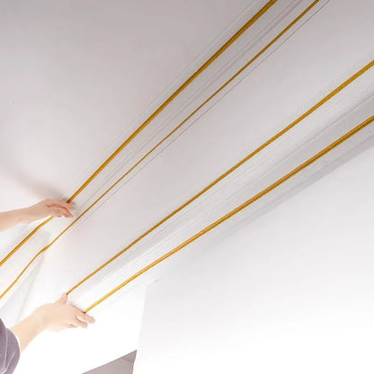 Two hands fit self-adhesive strips with gold lines along the top edge of a ceiling