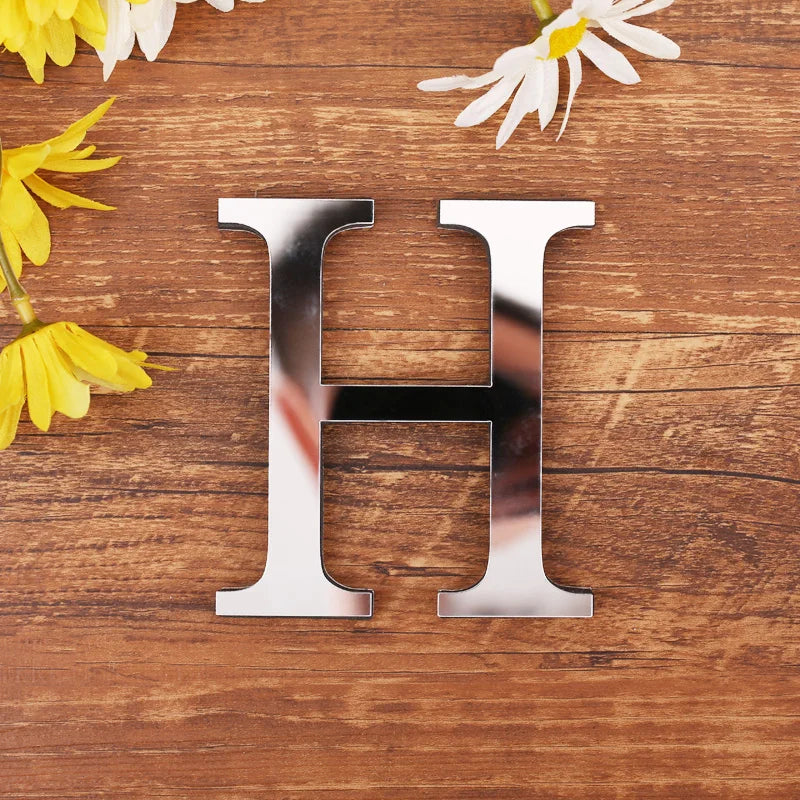 Letter H in silver mirror acrylic, 20 cm, on a wooden table with flowers