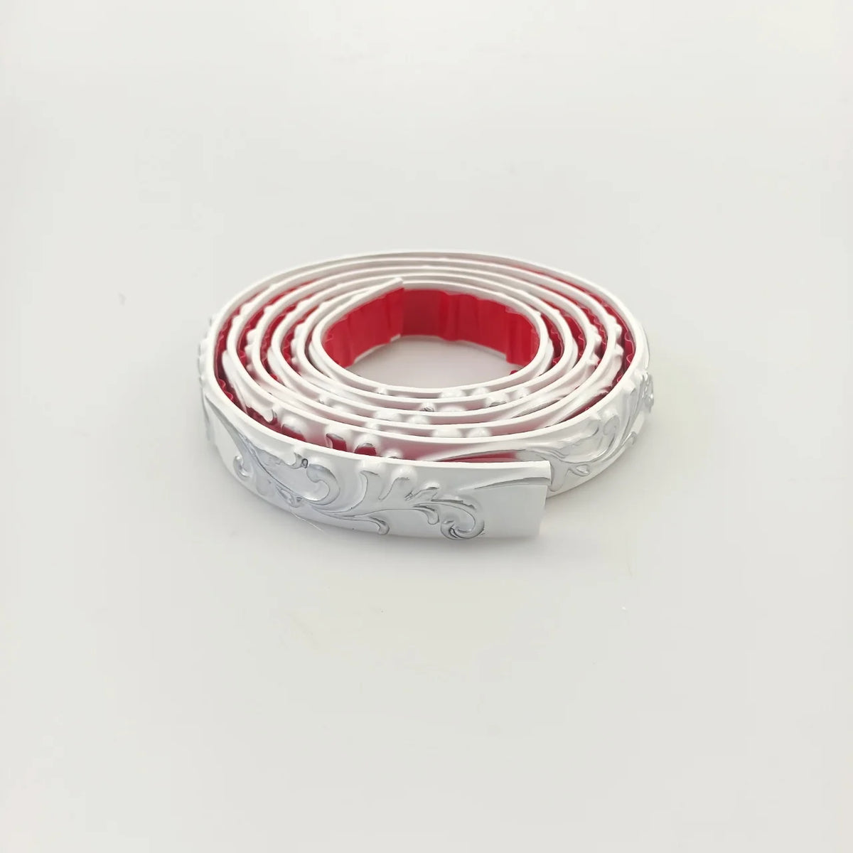White decorative moulding with silver decoration, rolled up, with the red adhesive back visible