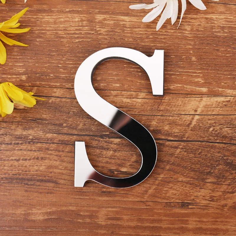 Letter S in silver mirror acrylic, 20 cm, on a wooden table with flowers