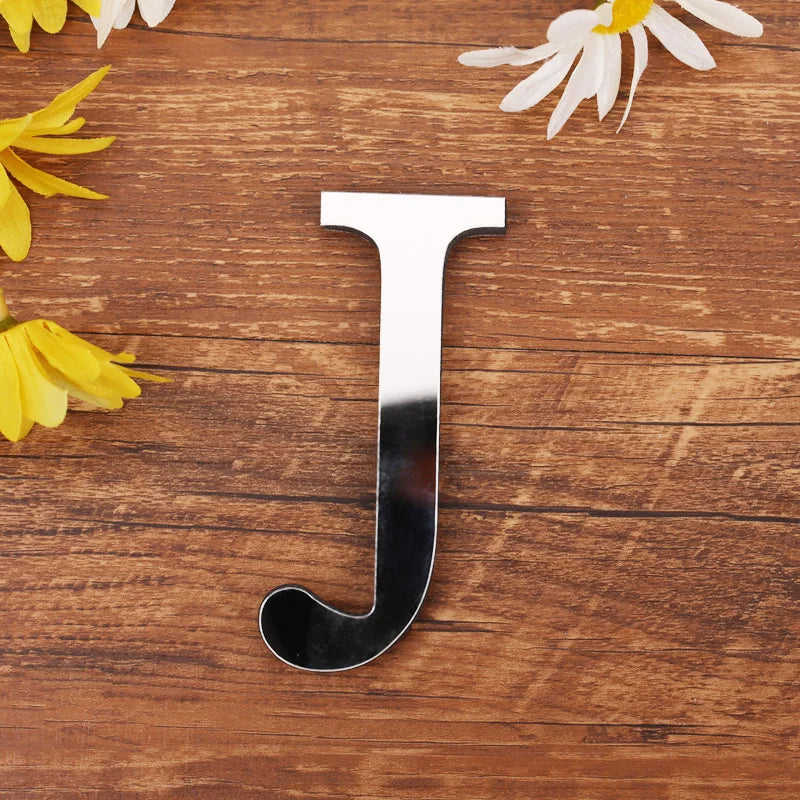 Letter J in silver mirror acrylic, 20 cm, on a wooden table with flowers