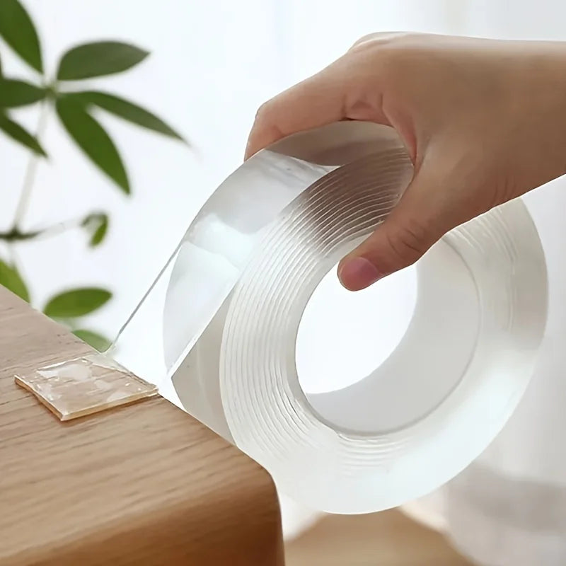 Roll of transparent double-sided tape on a wooden table with a piece already stuck down