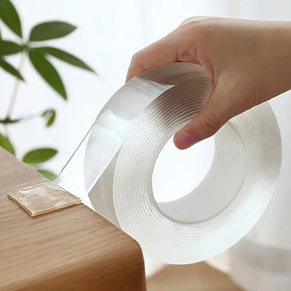 Roll of transparent double-sided tape on a wooden table with a piece already stuck down