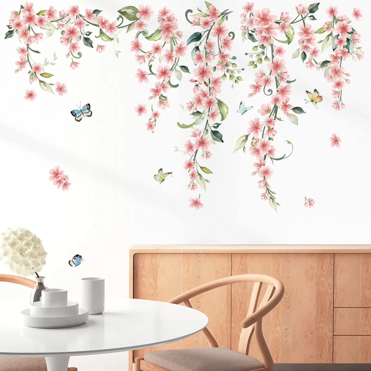 Roze bloeiende takken op de muur geplakt, van boven naar beneden vallend op een witte muur boven een houten dressoir