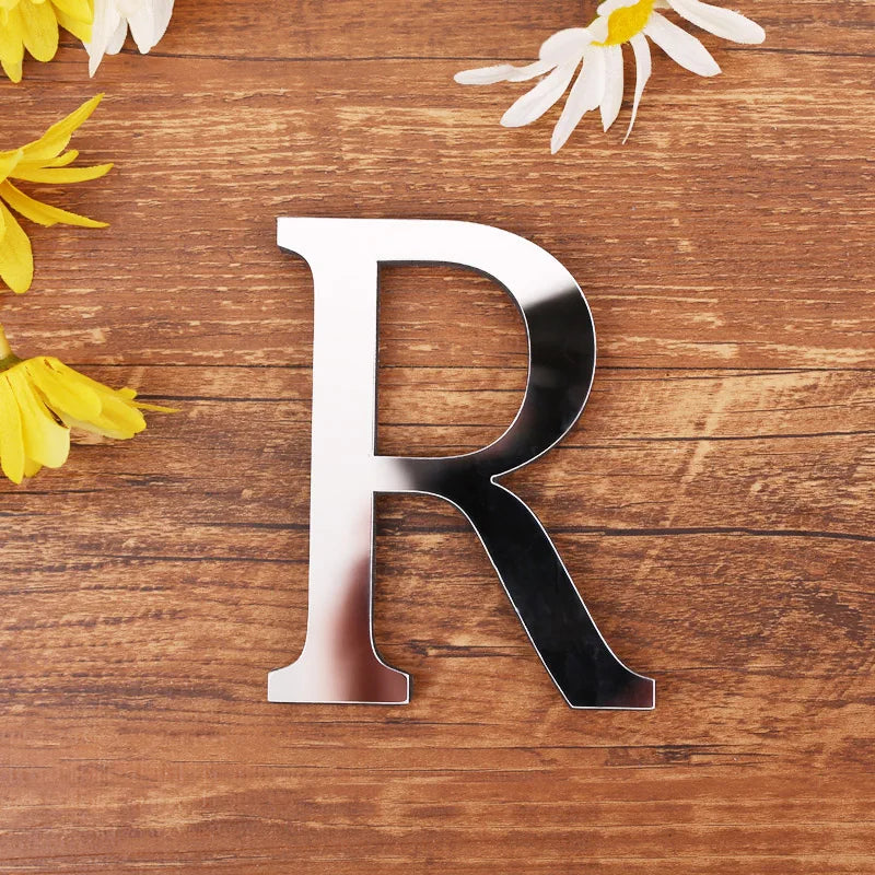 Letter R in silver mirror acrylic, 20 cm, on a wooden table with flowers