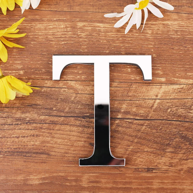 Letter T in silver mirror acrylic, 20 cm, on a wooden table with flowers