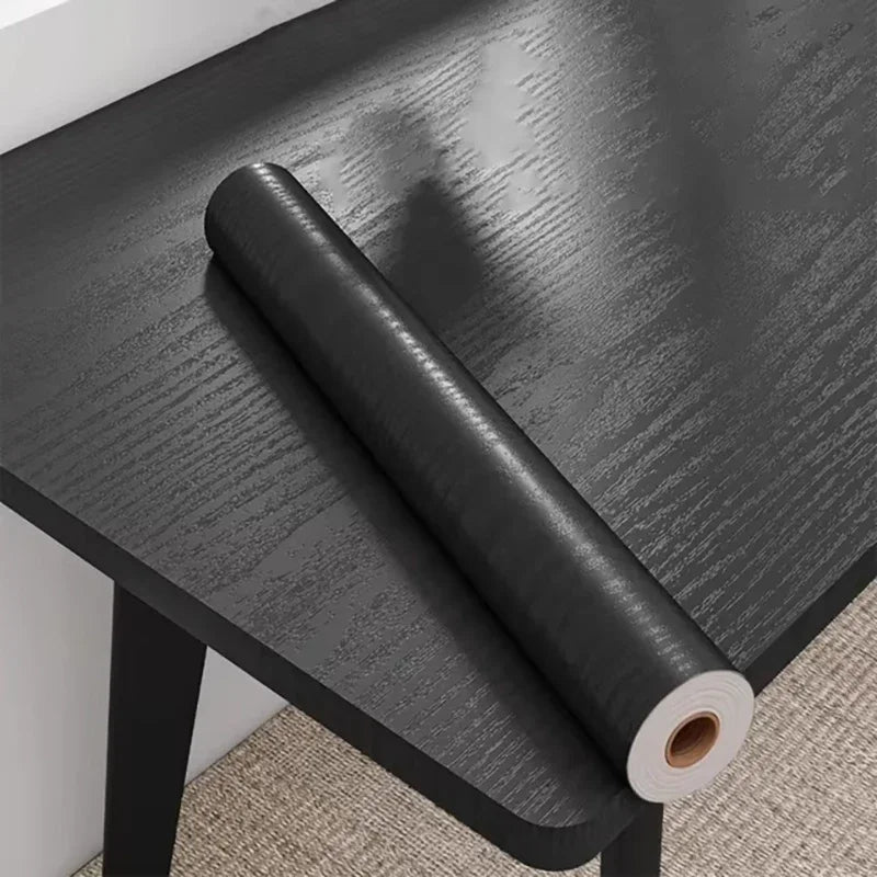 Roll of black wood effect adhesive vinyl resting on a table covered in the same vinyl