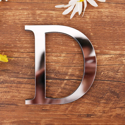 Letter D in silver mirror acrylic, 20 cm, on a wooden table with flowers