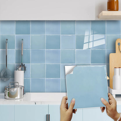Light blue square sticker with the back paper half peeled, in front of a wall of blue squares