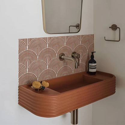 Terracotta hanging washbasin with the wall behind it covered in terracotta arch stickers, under a mirror