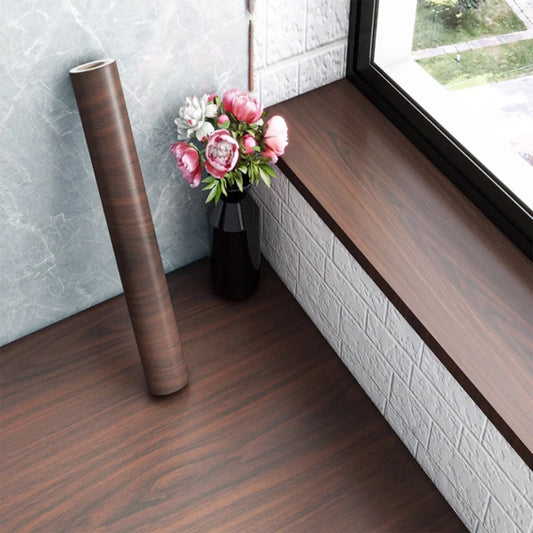 Roll of dark walnut effect self-adhesive vinyl next to a windowsill covered with the same vinyl