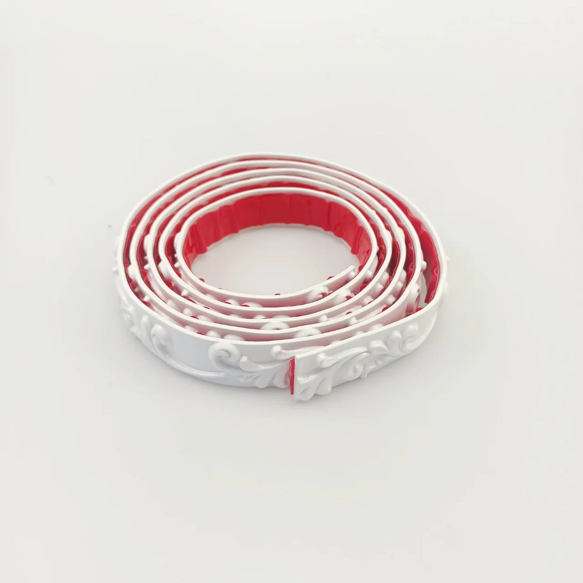 White decorative moulding rolled up, seen from above with the red adhesive back