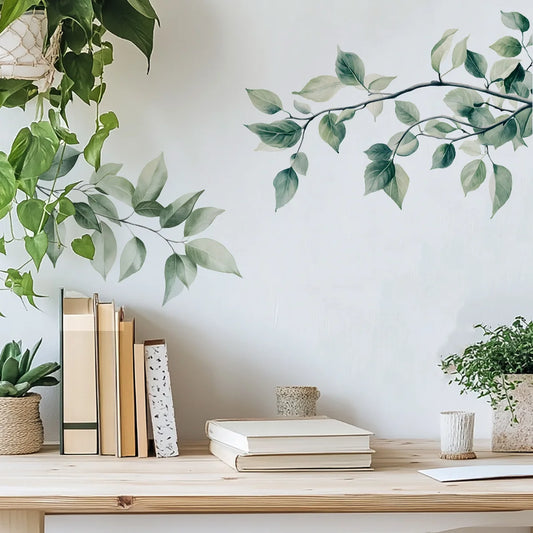 Muursticker met takken met groene bladeren boven een tafel met boeken en een plant
