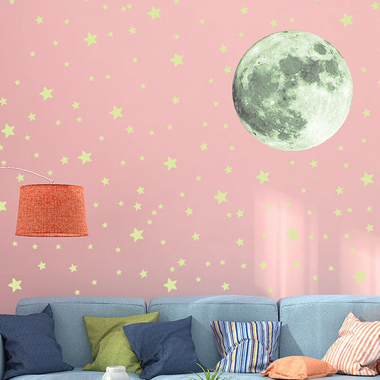 Vaaleanpunainen seinä, jolla kuutarra ja vaaleankeltaisia tähtiä vaaleansinisen, tyynyillä varustetun sohvan ja oranssin lampun yläpuolella