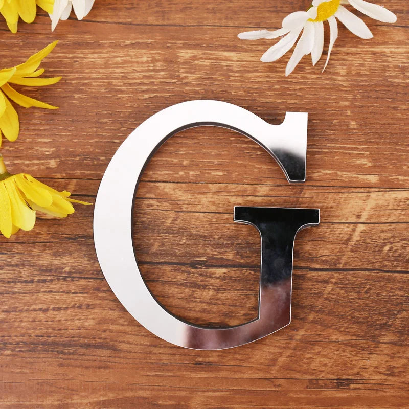 Letter G in silver mirror acrylic, 20 cm, on a wooden table with flowers