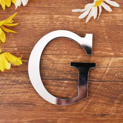 Letter G in silver mirror acrylic, 20 cm, on a wooden table with flowers