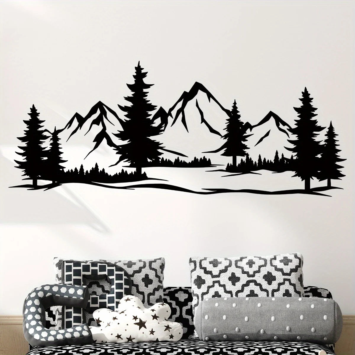 Black mountain and pine silhouette above a sofa with black and white patterned cushions