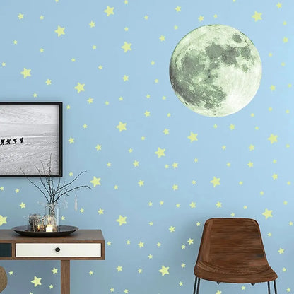 Light blue wall by day with a 20 cm moon and pale yellow stars, beside a small table and a brown chair