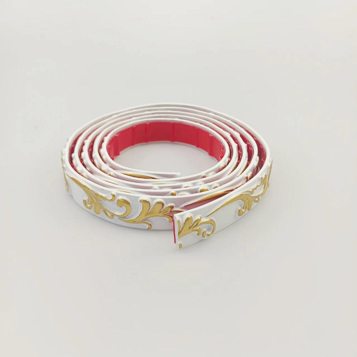 White decorative moulding with gold decoration, rolled up, with the red adhesive back visible