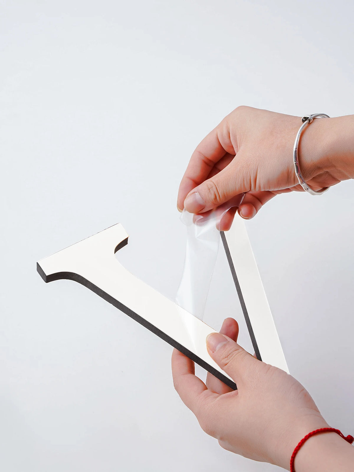 Hands peeling the protective film off a mirror effect letter V on a white background