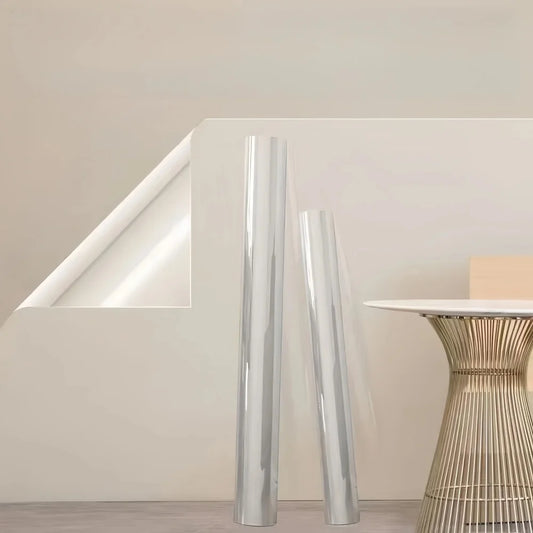 Zwei Rollen transparente Schutzfolie und eine abgelöste Ecke der Folie an einer hellen Wand