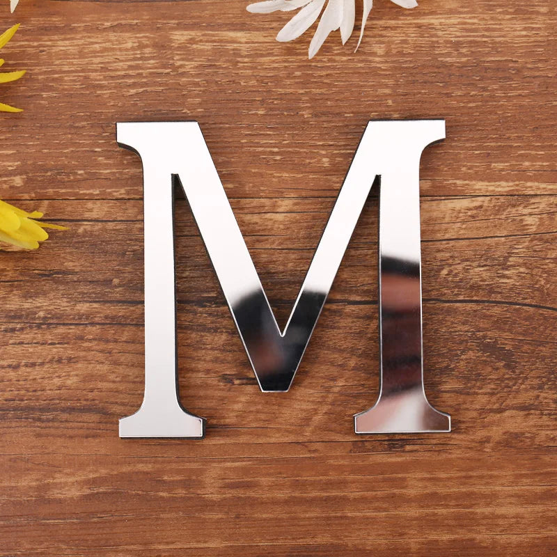 Letter M in silver mirror acrylic, 20 cm, on a wooden table with flowers