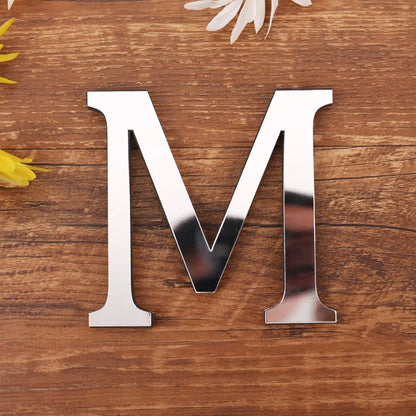 Letter M in silver mirror acrylic, 20 cm, on a wooden table with flowers
