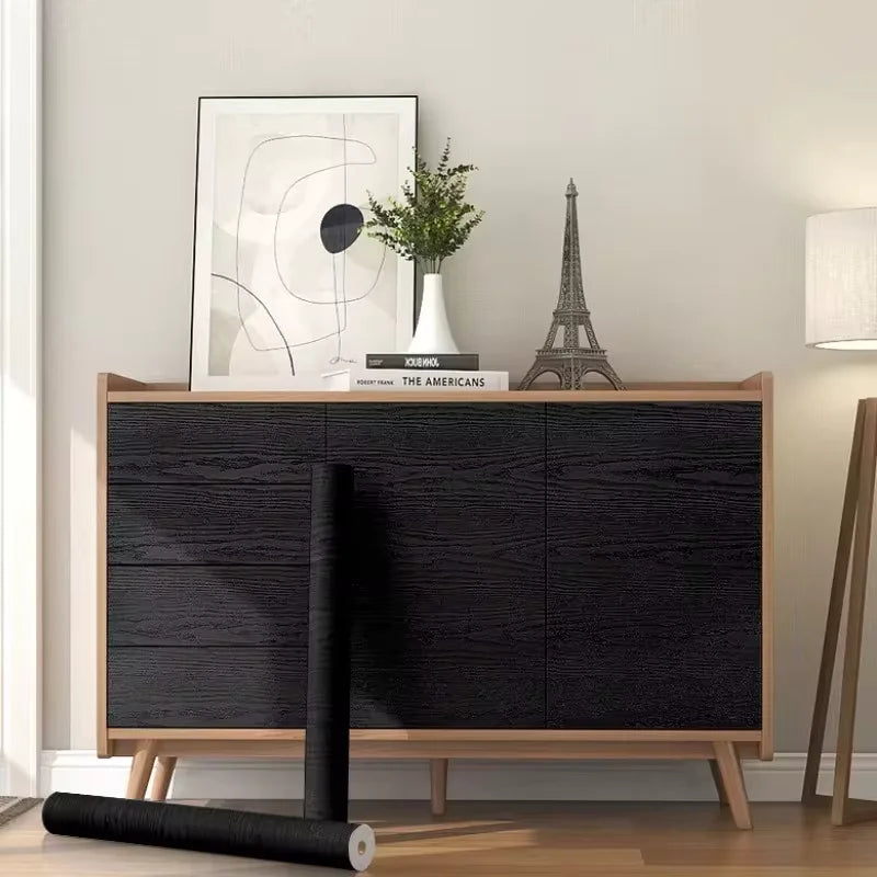 Sideboard covered in black wood effect adhesive vinyl, with a roll at the foot of the furniture