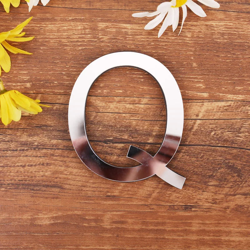 Letter Q in silver mirror acrylic, 20 cm, on a wooden table with flowers