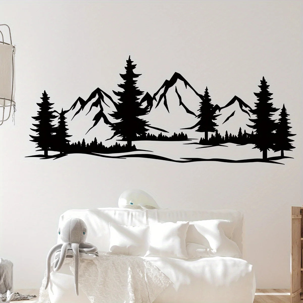 Black mountain and pine silhouette on a beige wall above a white bed with a soft toy